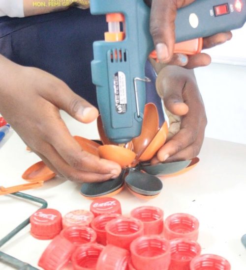 A student of the Waste Rescue Club constructing upcycled arts with support from a trainer from trashed plastic bottle covers and discarded plastic spoon Photo: Solomon Eko